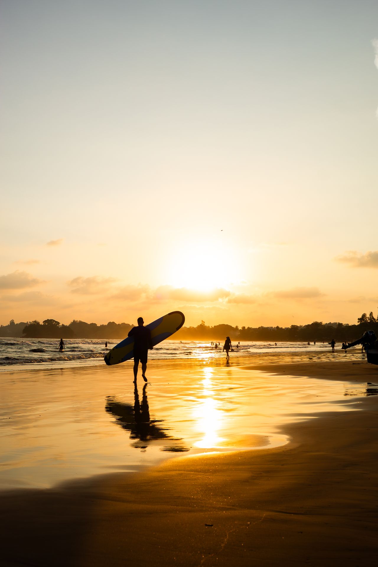 Surfer walking along Weligama Beach at sunset